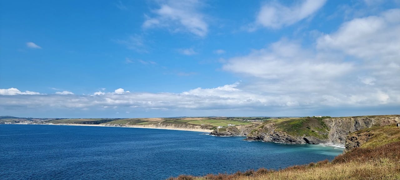 Home Panoramic view of a coastline with bright blue ocean and rocky cliffs under a clear sky.